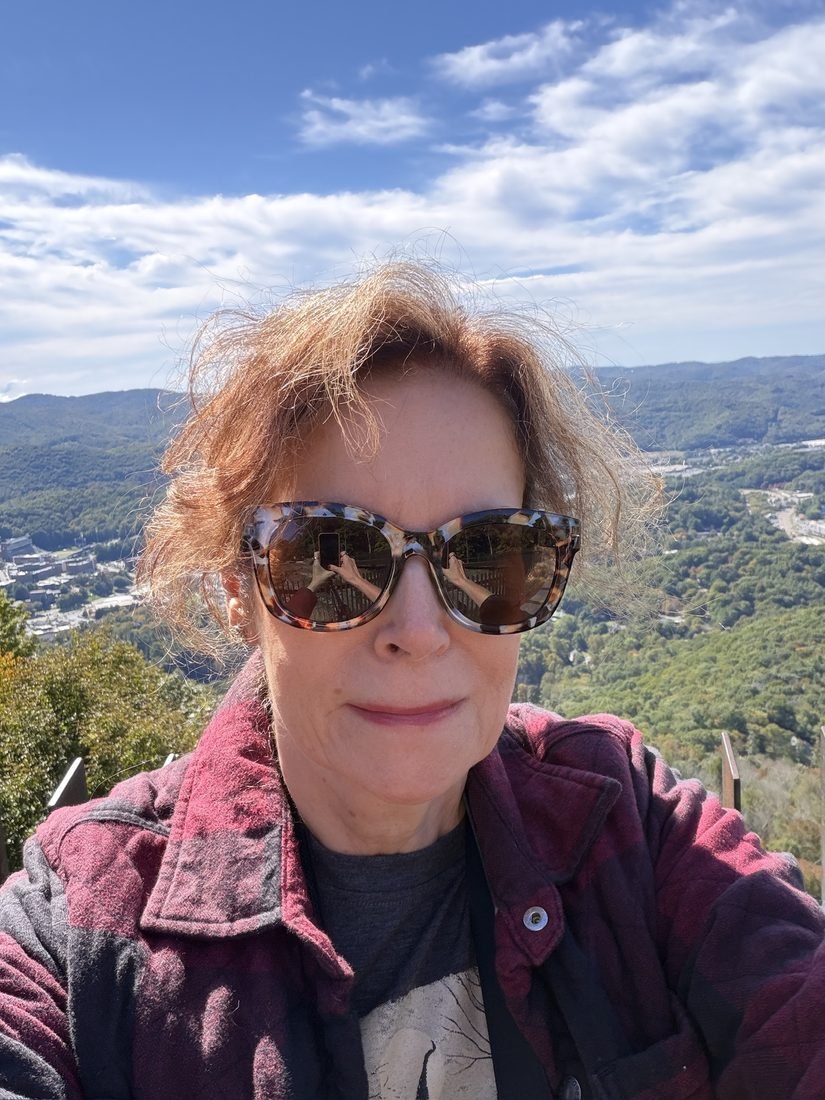 Barbara Rozgonyi in sunglasses and a plaid jacket, windblown, with the Boone valley behind her