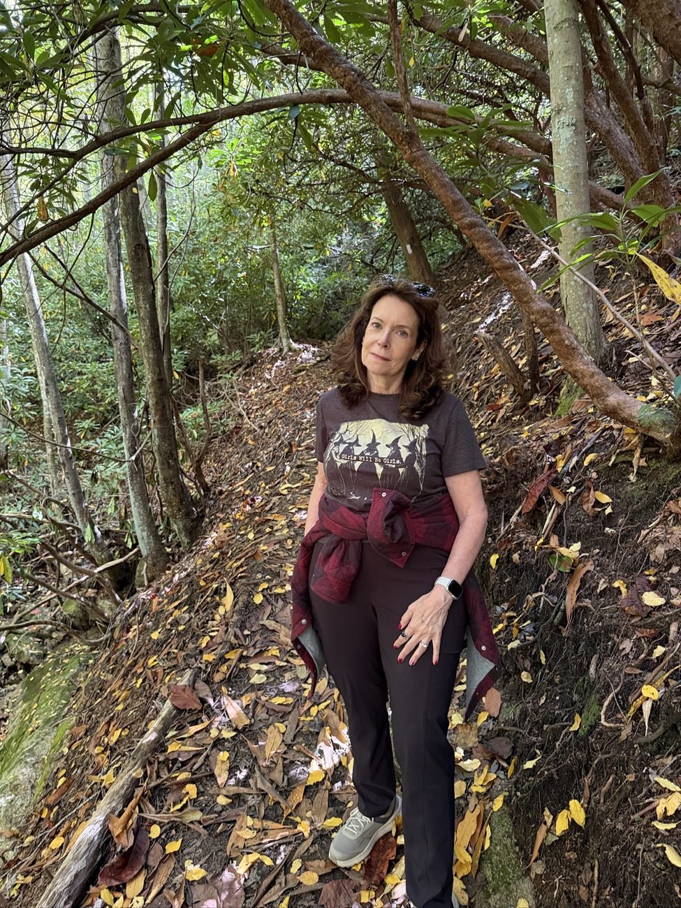 Barbara Rozgonyi standing on a leaf-covered woodland trail under rhododendrons on Beech Mountain