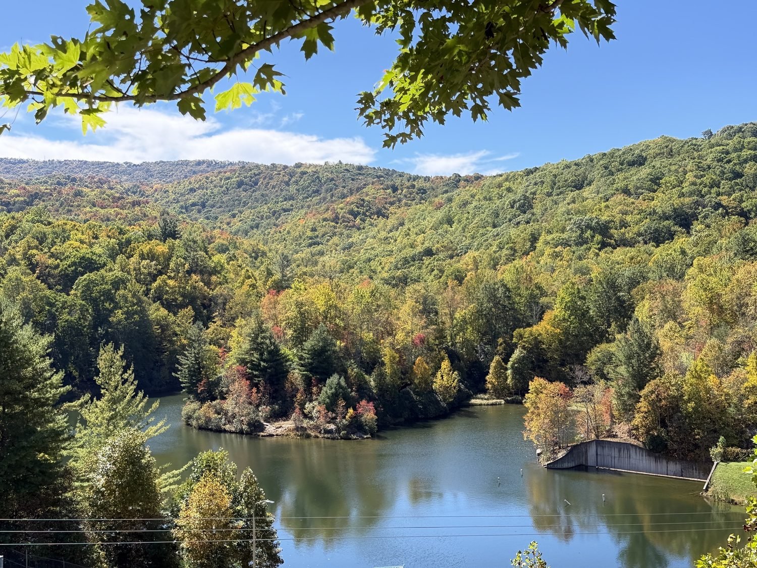 Mountain lake and forested hills seen through oak leaves from an overlook on Beech Mountain, early October