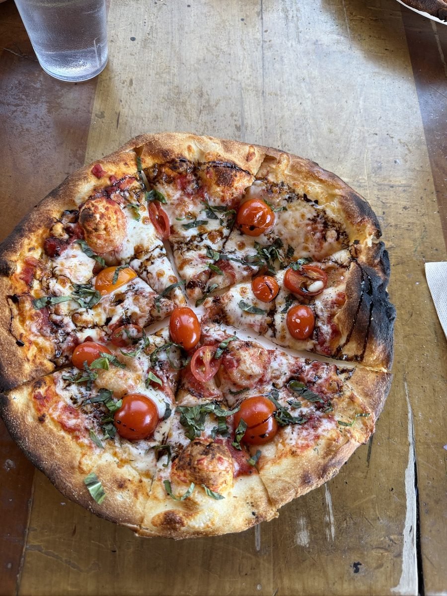 Wood-fired pizza with cherry tomatoes, basil and balsamic glaze on a wooden table