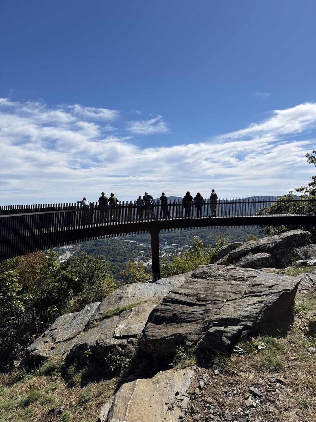 Visitors standing on the curved steel Howard Knob overlook above Boone, North Carolina, under a deep blue sky
